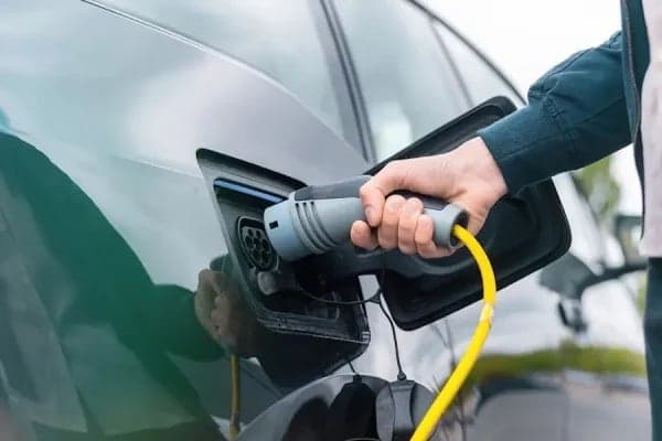 A driver connecting a charging cable to the port of an electric car